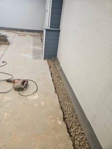 Interior basement waterproofing system installation showing a perimeter drainage trench with clean gravel before the concrete floor is restored.
